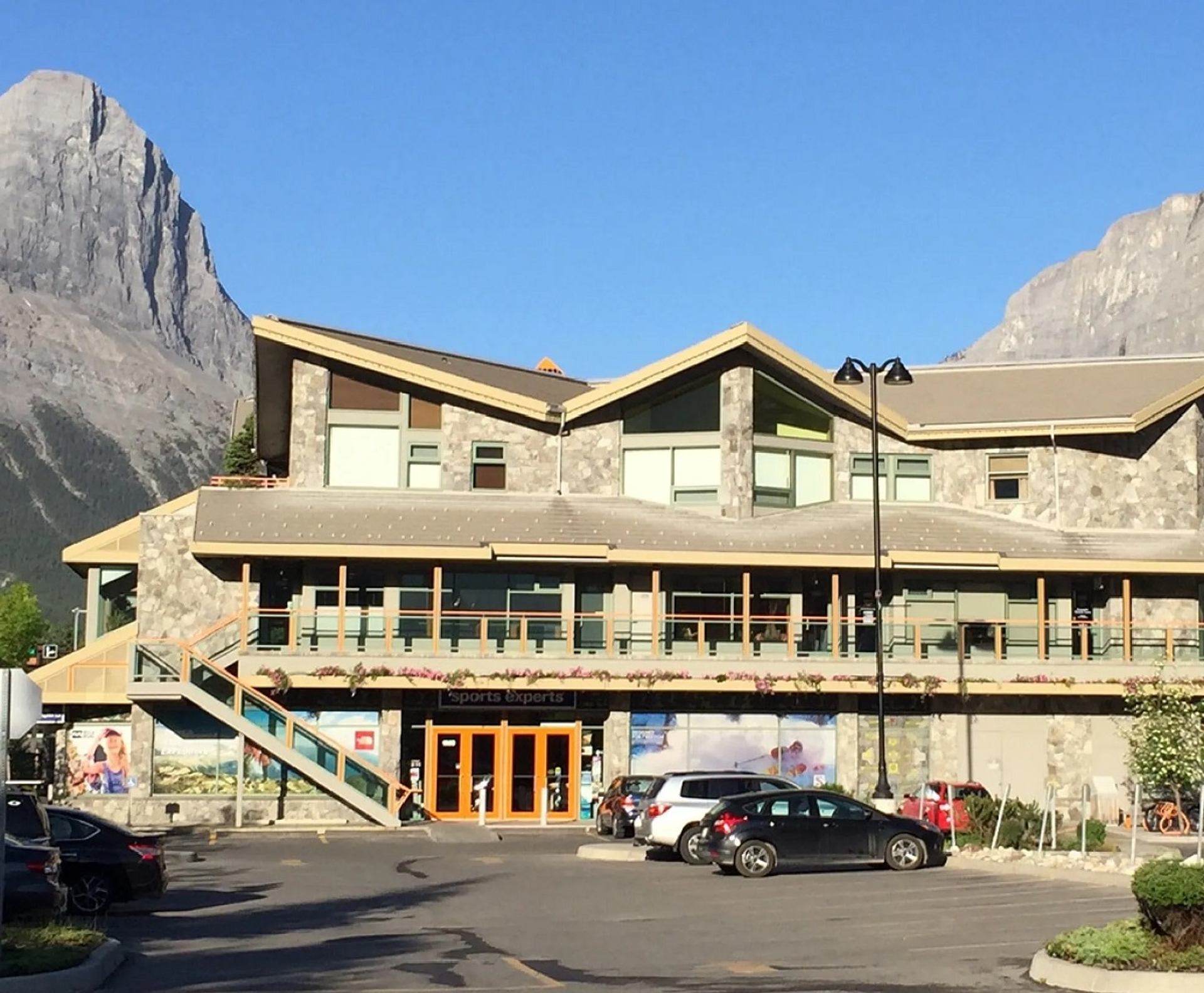 Modern stone building with mountain peaks in the background and cars parked out front.