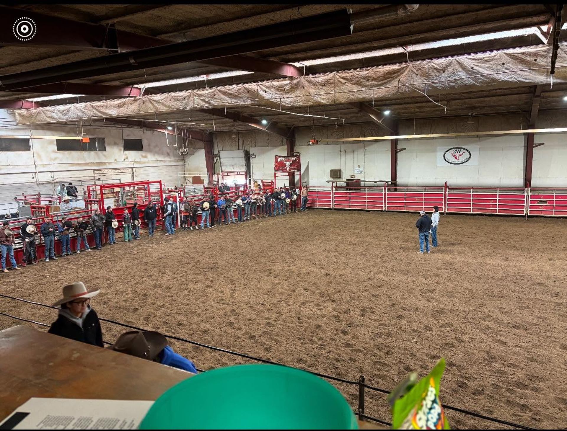 Indoor rodeo arena with people lined along red chutes and two figures standing centre.