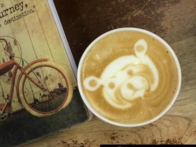 Latte with bear face art next to a book