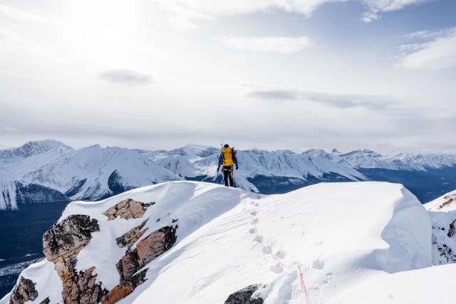 A lone person stands at the summit overlooking the mountains while ice climbing in Jasper National Park.