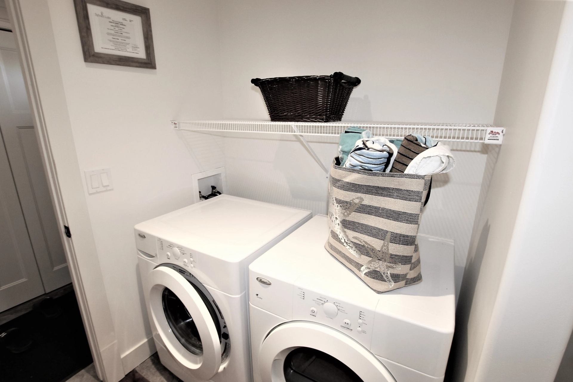 Laundry area with front-load washer and dryer, shelf, and storage basket.