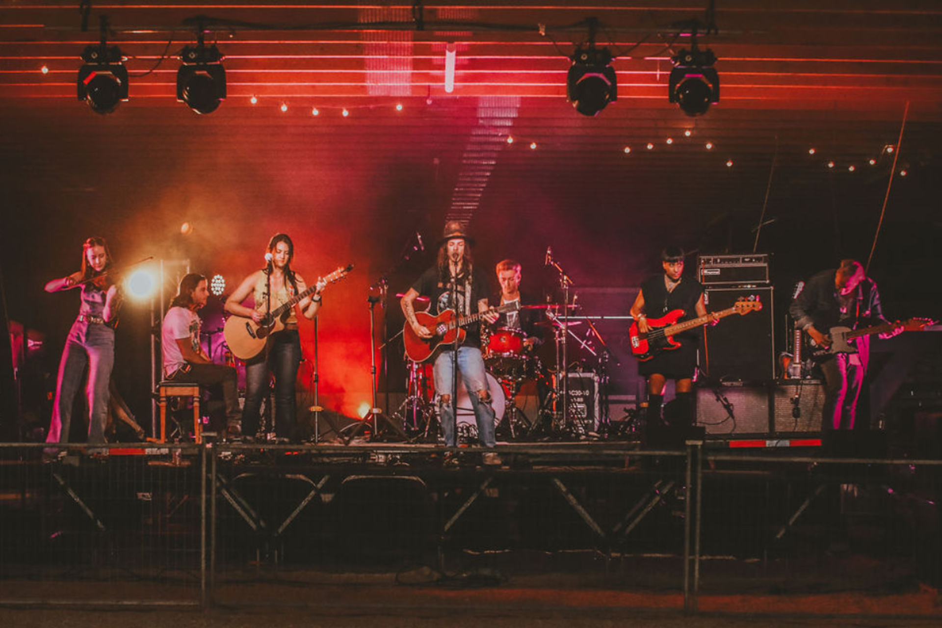 A 7 piece band tests the sound on stage under red and purple lights. 