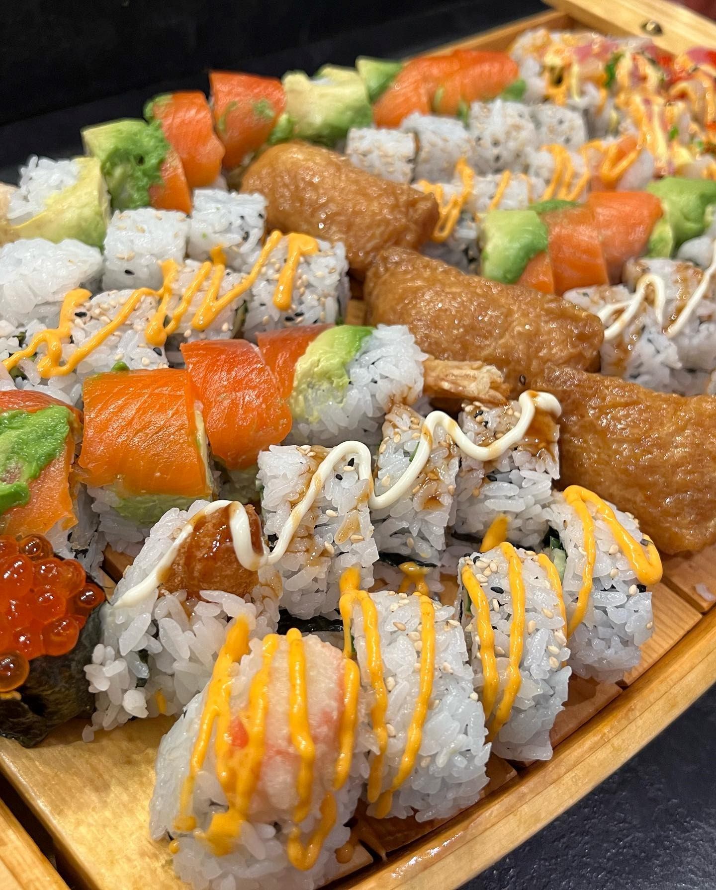 Assorted sushi rolls with salmon, avocado and sauces on a wooden tray.