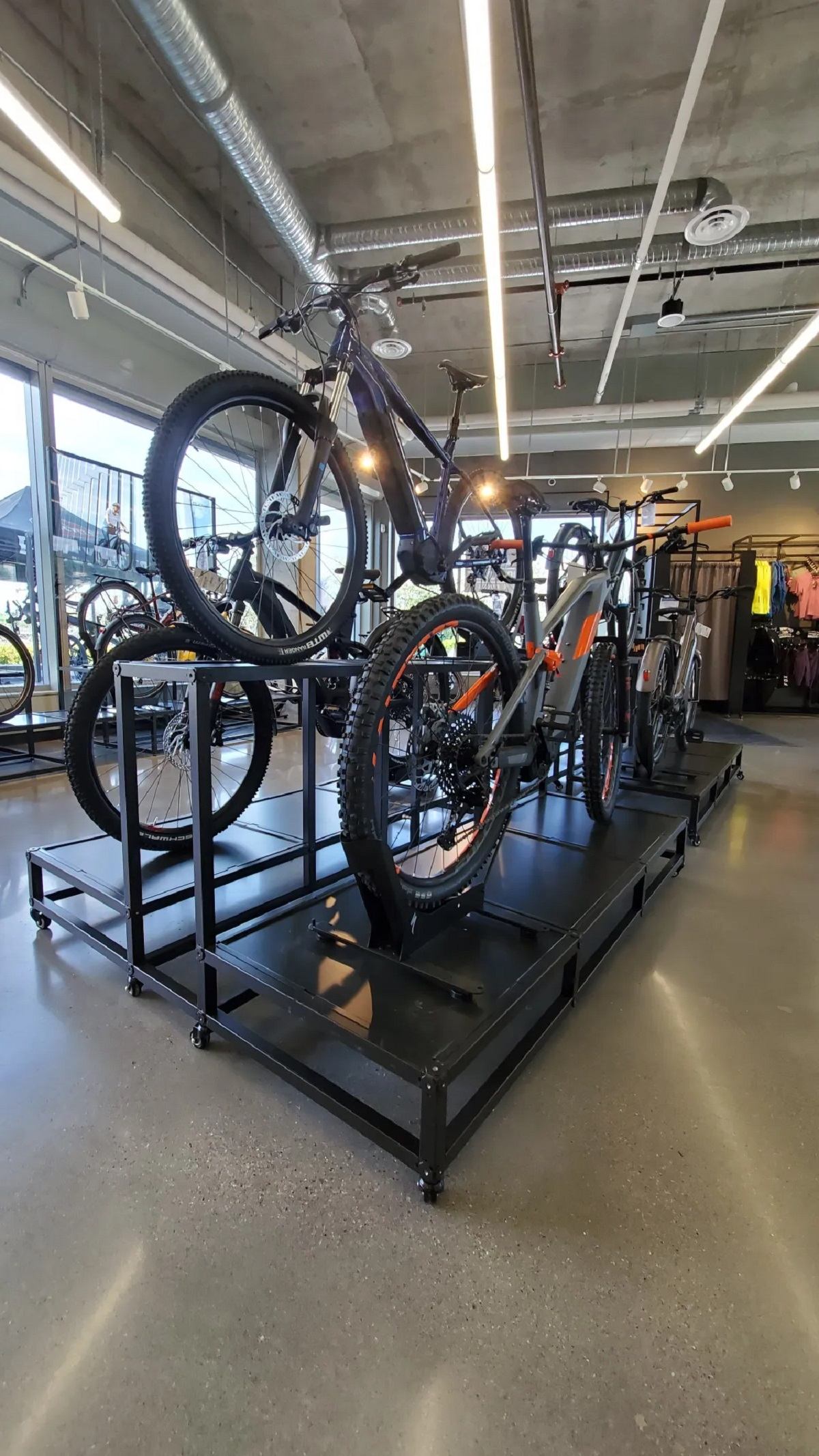 Bikes on tiered rack in modern shop with concrete floors and large windows.