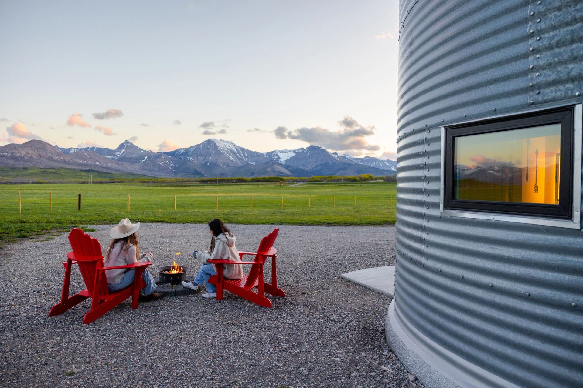 Two young women sitting around fire overlooking mountains at Twin Butte Silos during blue hour.