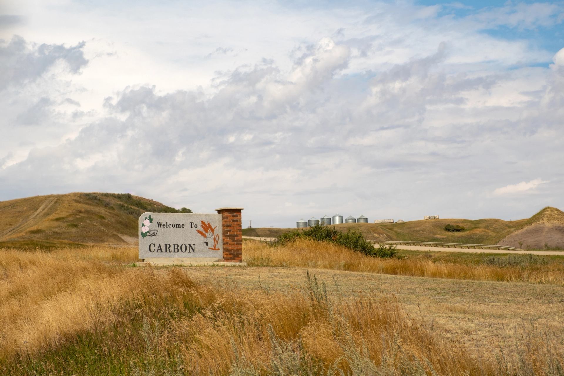 Welcome sign for Carbon with rolling hills and silos in the background.