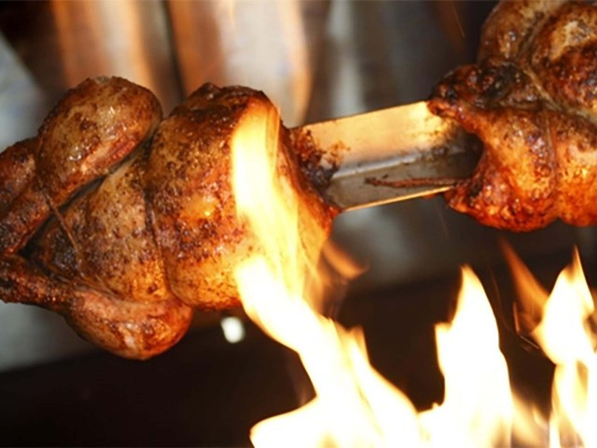 Rotisserie chicken roasting over open flame at upscale steakhouse.