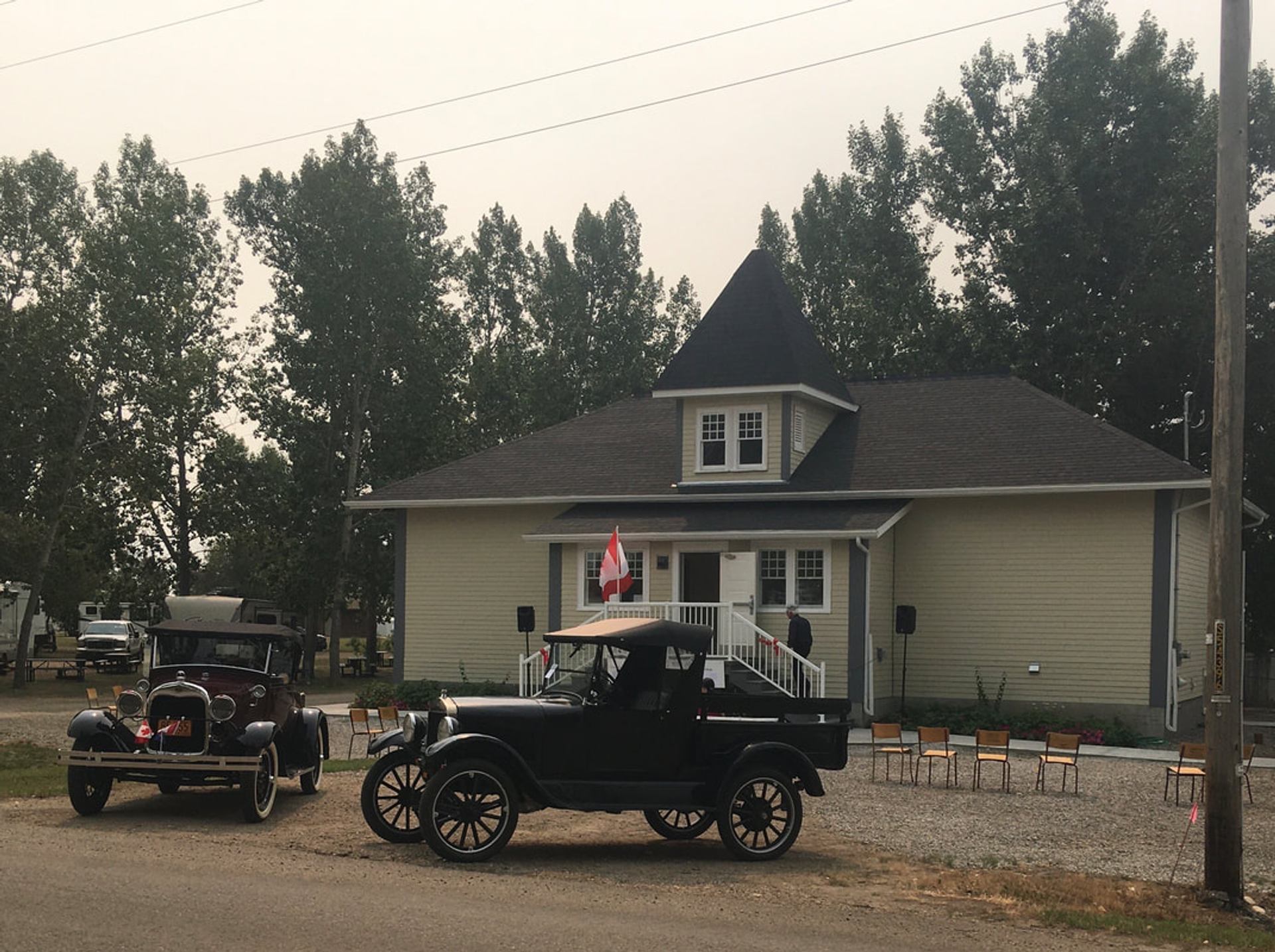 Two vintage vehicles are parked outside a heritage building surrounded by trees and seating.