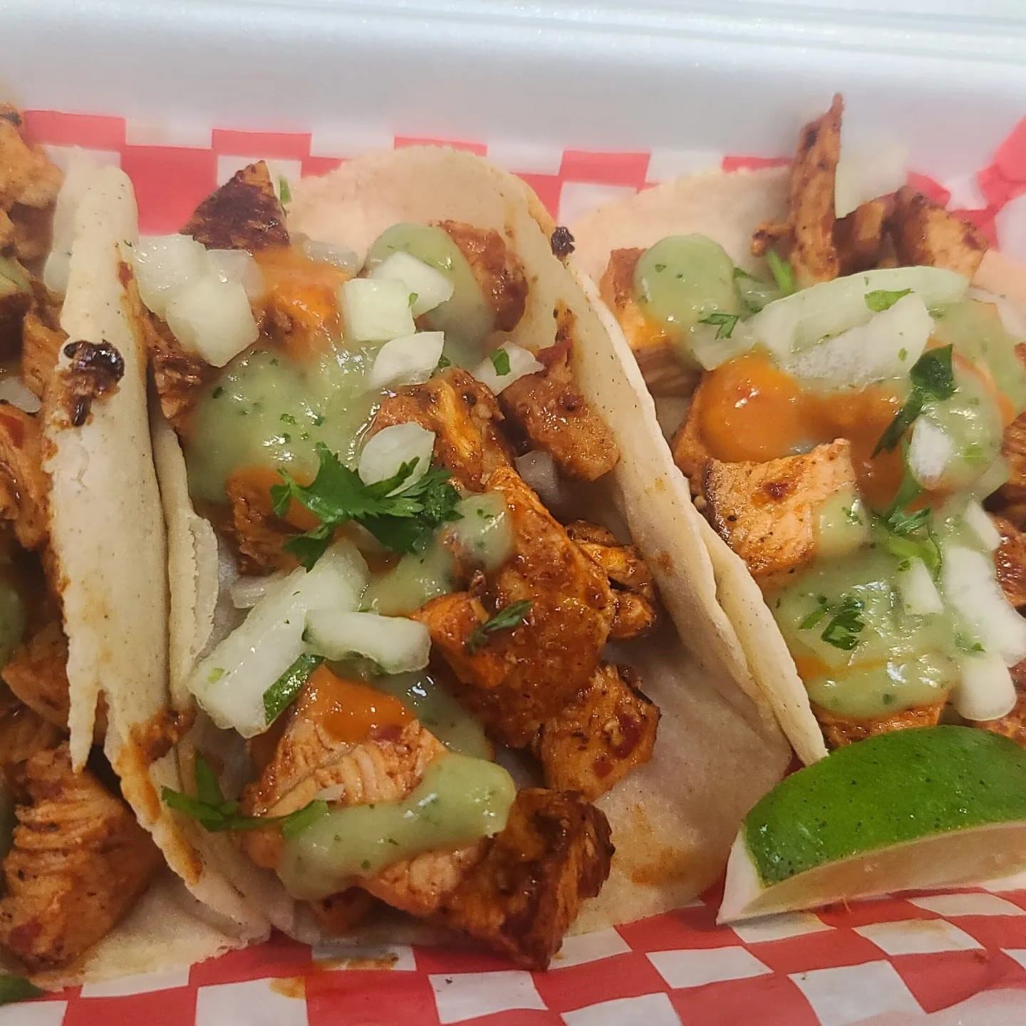 Two tacos with grilled meat, onions, cilantro, salsa and lime wedge in takeout box.