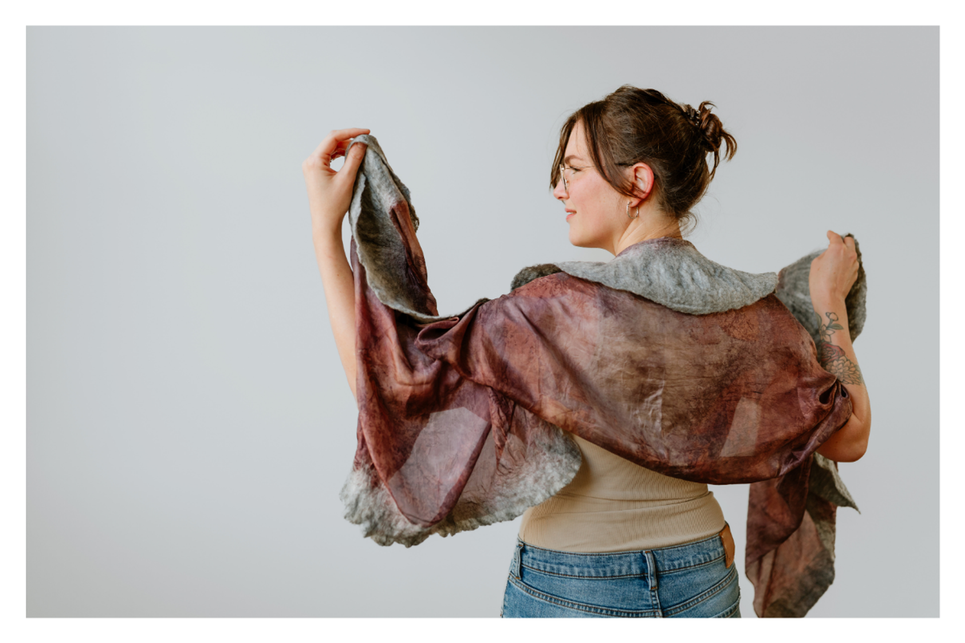 Person seen from behind holding a sheer, multicoloured shawl against a plain wall.
