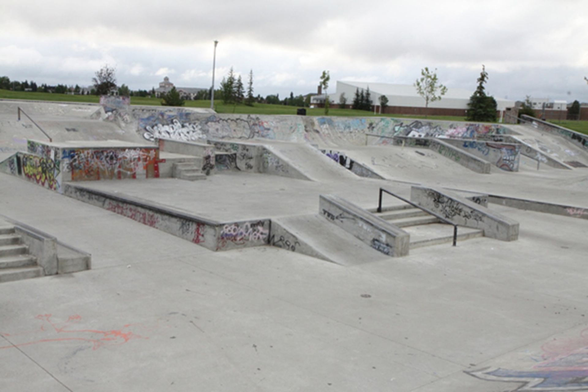 Concrete skate park with ramps, stairs and rails covered in graffiti, empty of people.