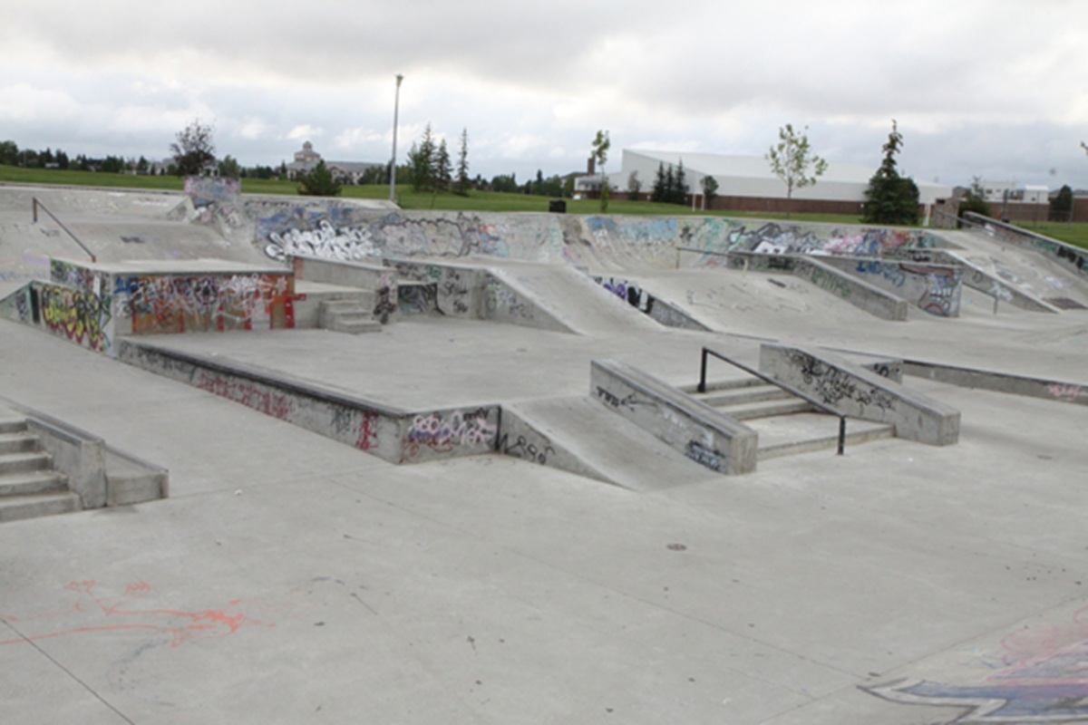 Concrete skate park with ramps, stairs and rails covered in graffiti, empty of people.