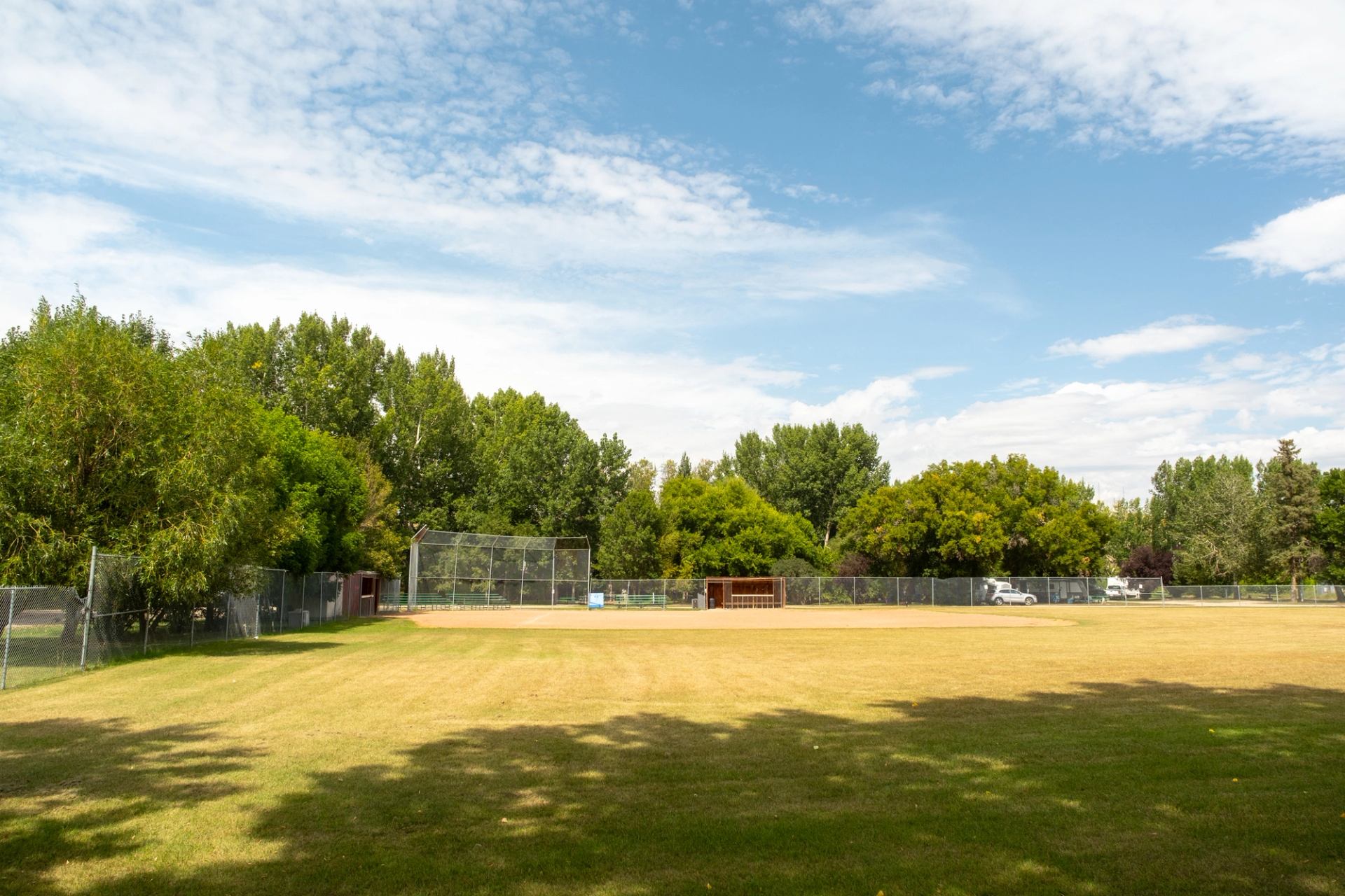 Open field with a baseball diamond, fence, and trees under a clear blue sky.