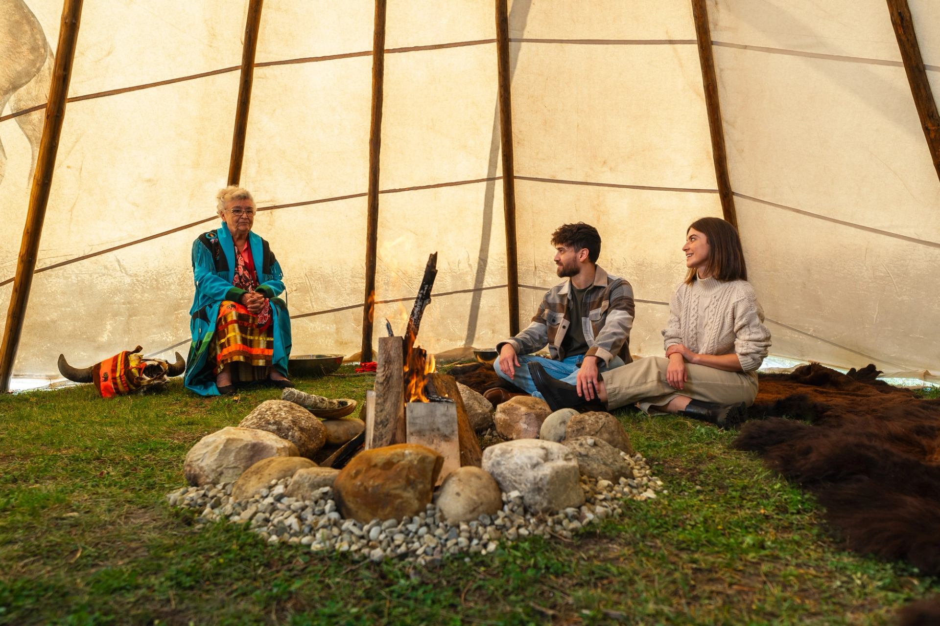 An elder in colourful clothing sits in a tipi with a man and woman.