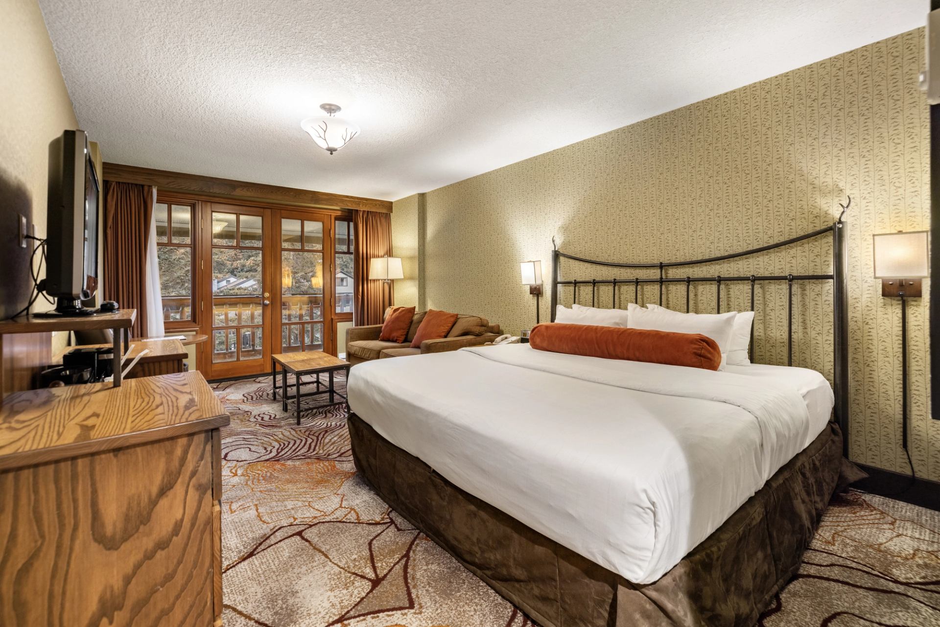 Hotel room with a king size bed, seating area, tv stand and a balcony.