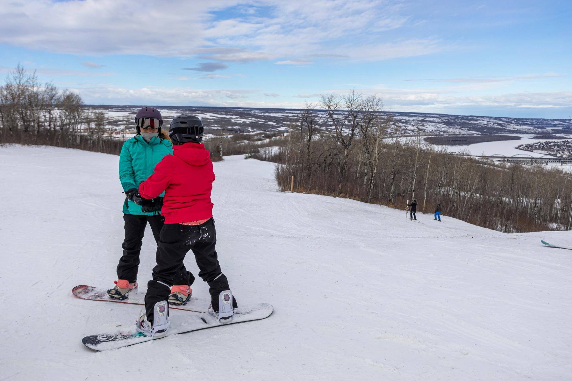 Two snowboarders hold hands while boarding at Misery Mountain Ski Area in Peace River