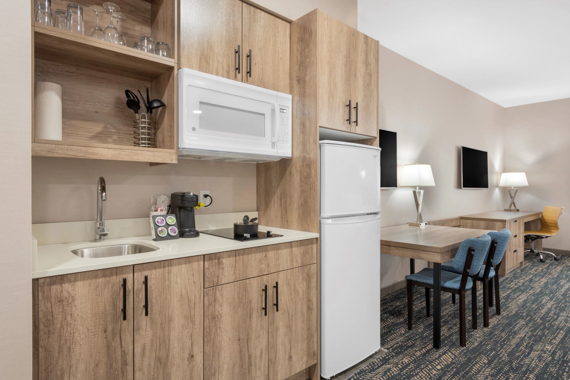 Hotel room with kitchenette, workspace, and dual TVs.