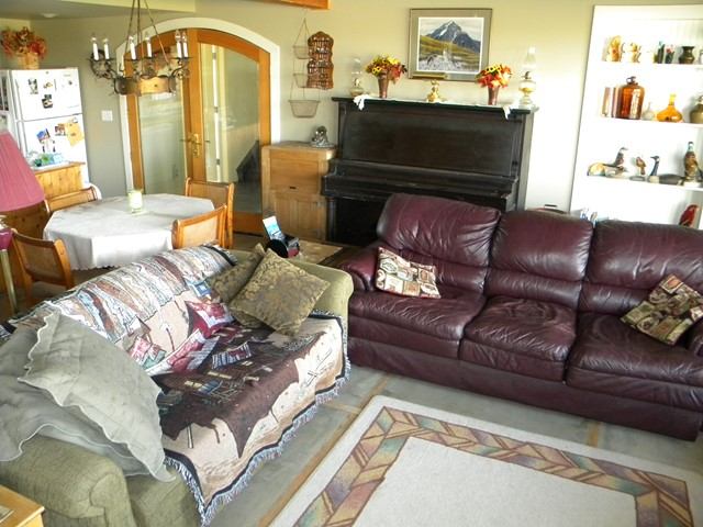 Living room with dark leather sofa, quilted beds, piano, and wall shelves in Rendezvous Ranch B&B.
