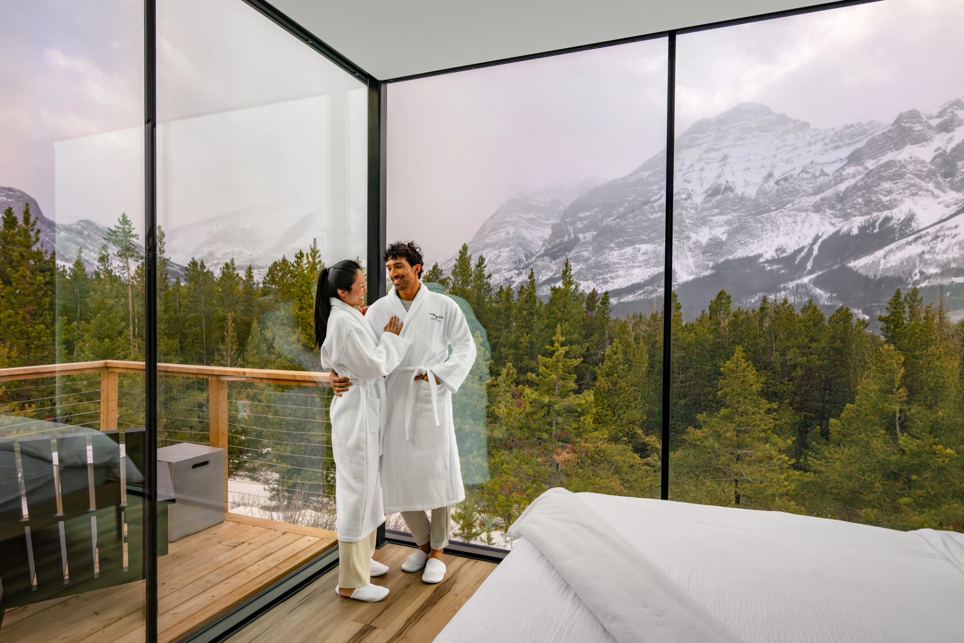 Two people in white robes stand by windows overlooking snowy mountains and forest.