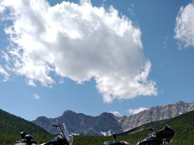 Motorcycles parked with mountain backdrop under blue sky.