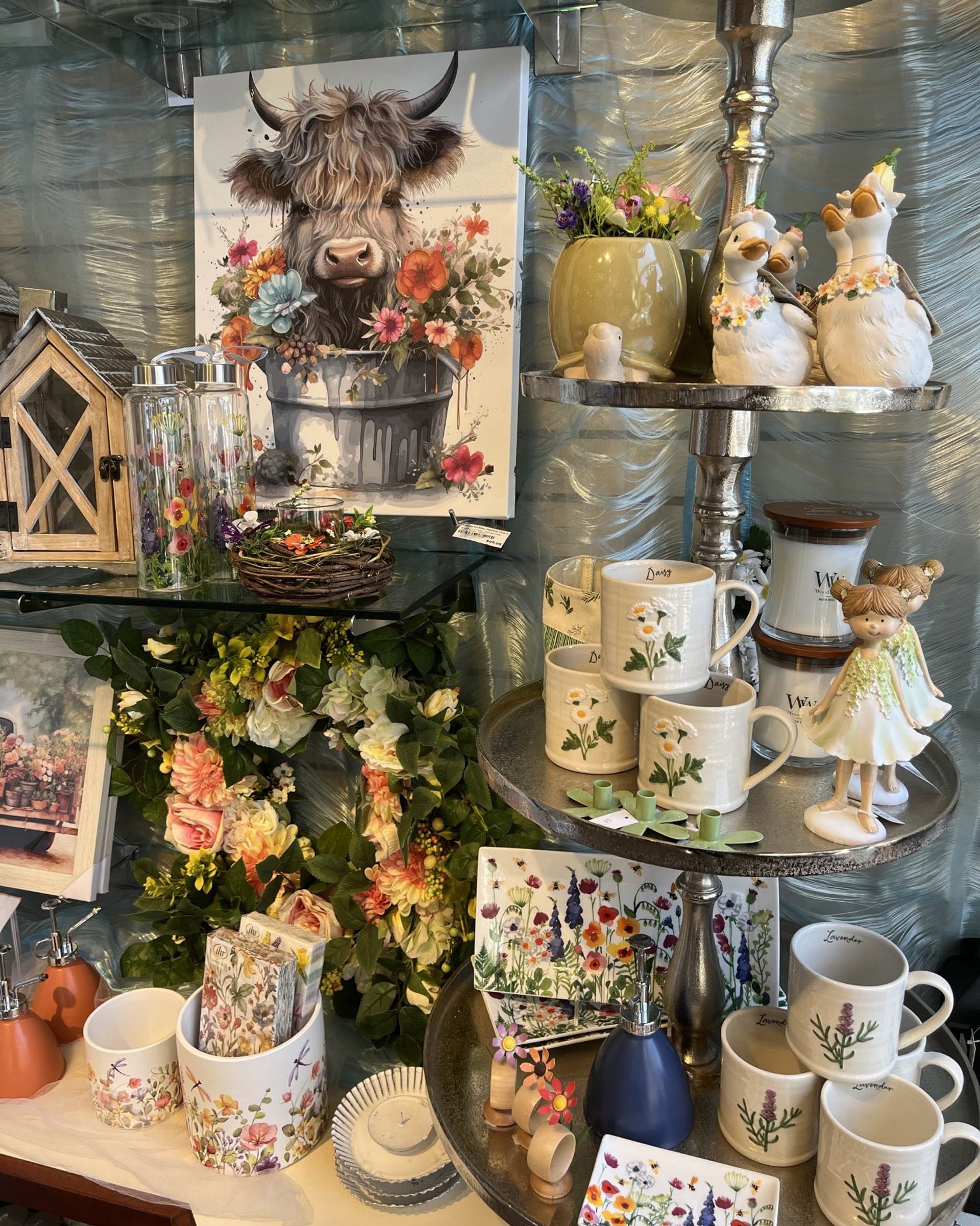Gift shop display with floral mugs, animal figurines and cow painting surrounded by flowers.