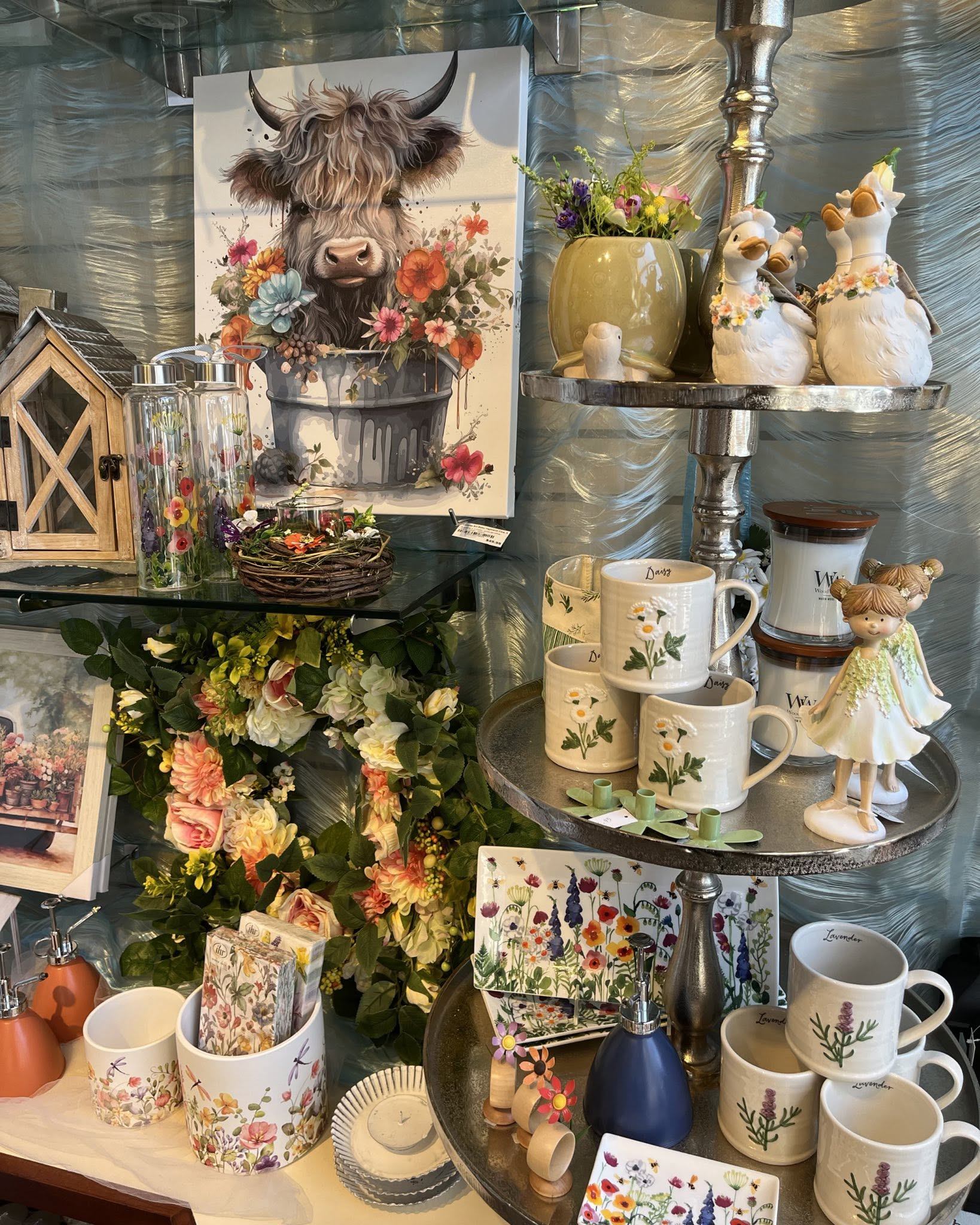 Gift shop display with floral mugs, animal figurines and cow painting surrounded by flowers.