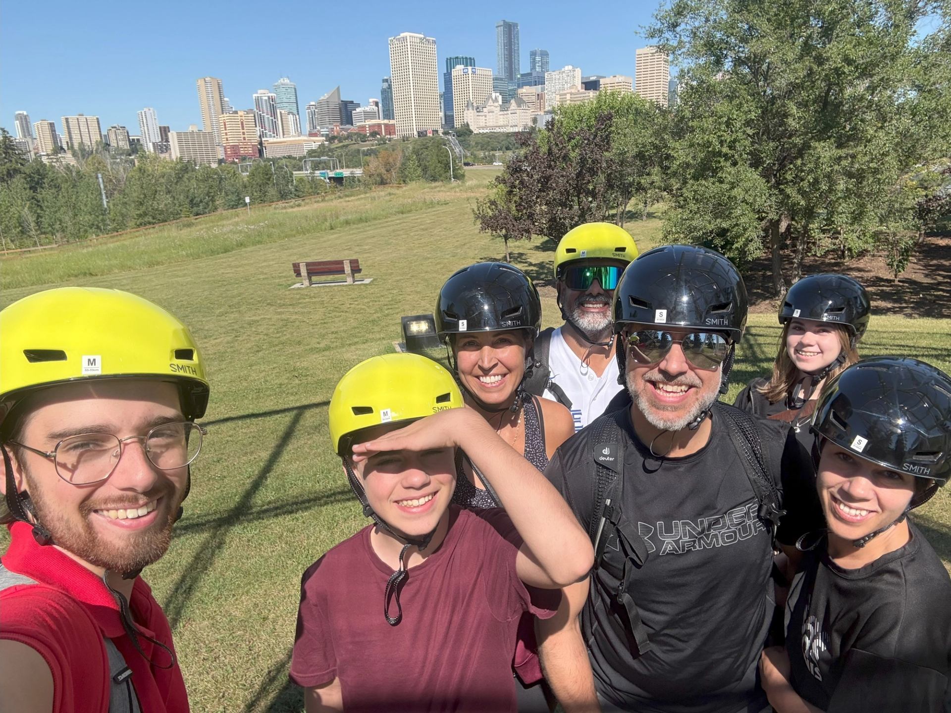 Group in helmets takes a selfie with city skyline in the background on grassy hill.
