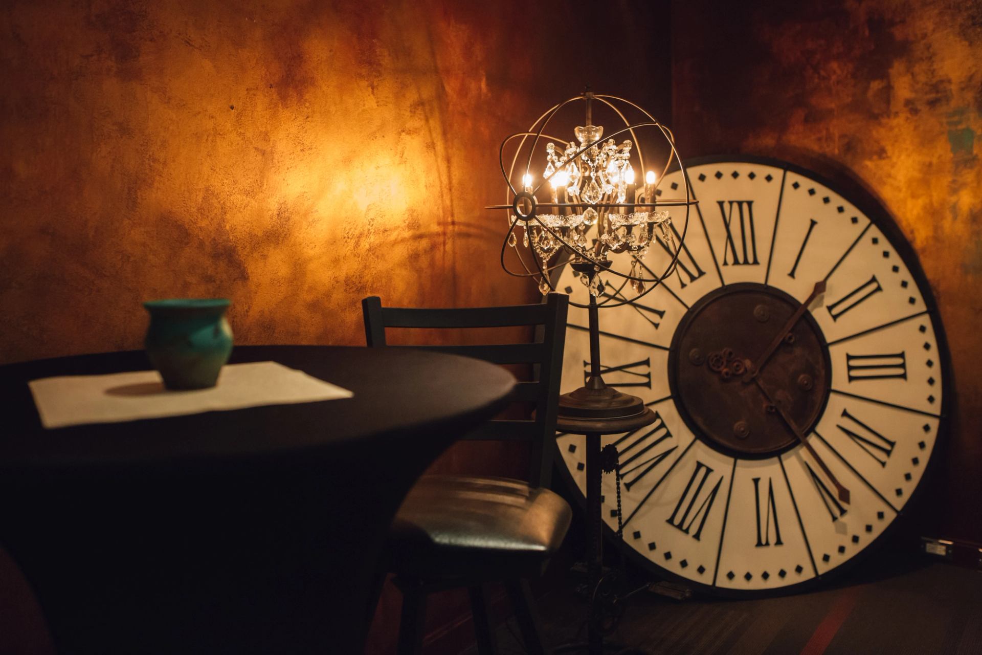 Round table with vase, chair, ornate lamp and large Roman numeral clock.