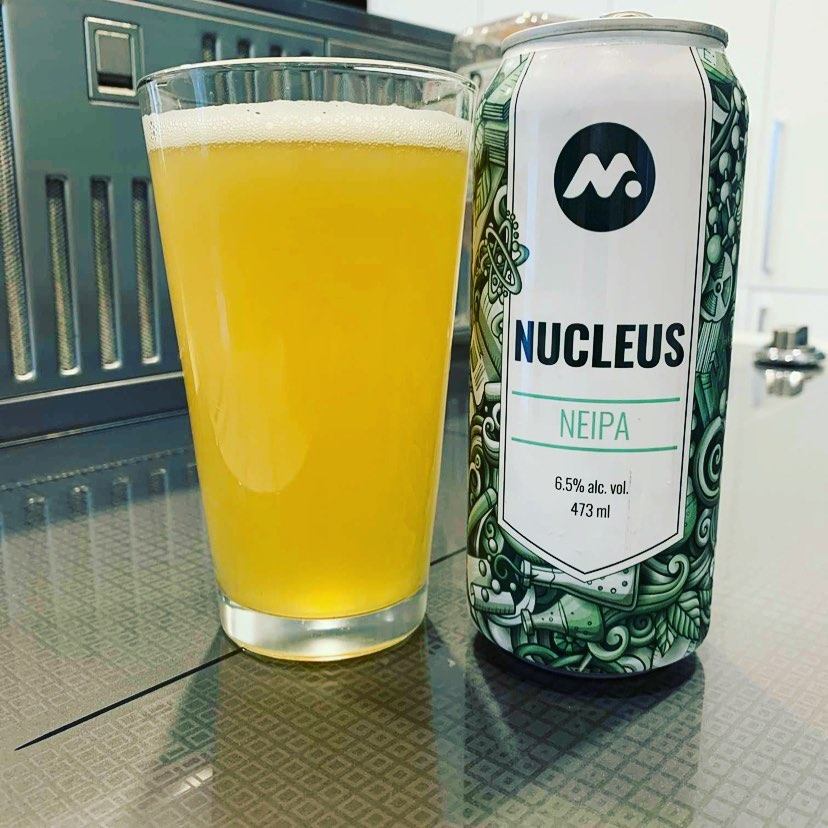 Glass of Nucleus NEIPA next to its can on a taproom counter.