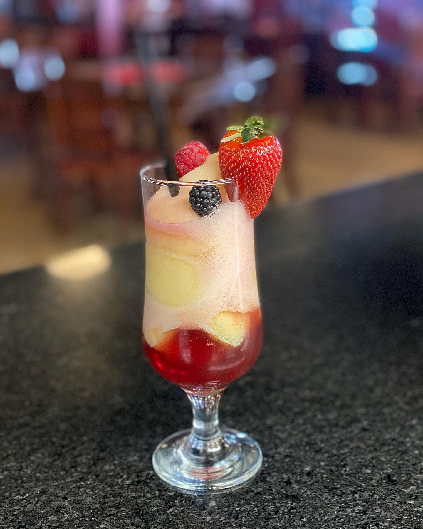 Tall glass of layered frozen drink topped with strawberries and berries