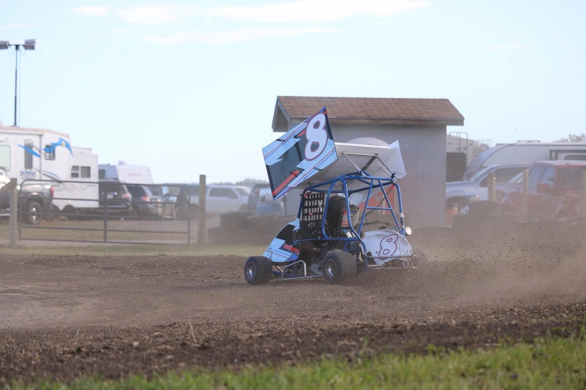 Mini sprint car kicking up dirt while racing alone on a dirt track.