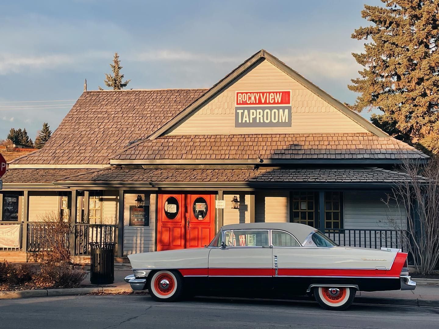 Exterior of Rocky View Brewing Company with red doors and an antique car parked in front.