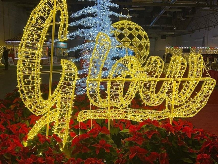 Glowing yellow “Glow” sign with poinsettias and a lit tree in the background.