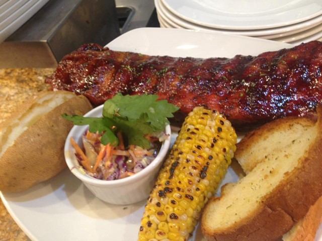 Plate of BBQ ribs with grilled corn, coleslaw, baked potato, and garlic toast.