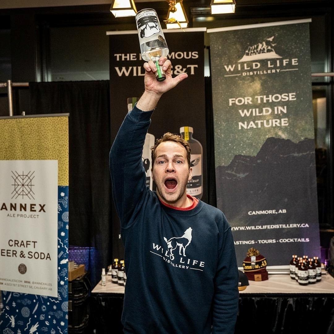 Person holding bottle up at indoor festival with Wild Life Distillery banner.