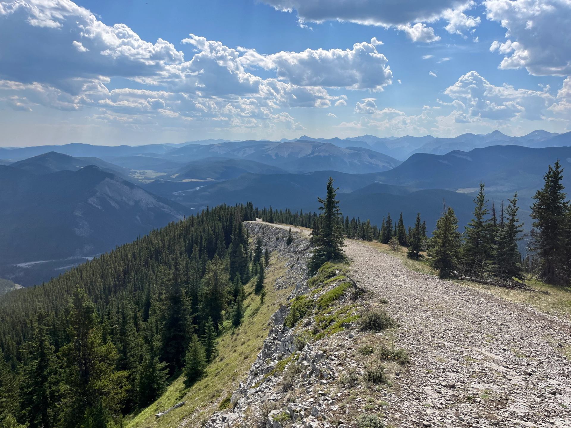 Scenic ridge trail overlooking forested valleys and distant mountain ranges.