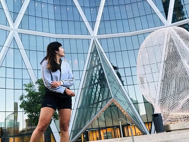 Person stands outside glass building beside large spherical light sculpture.