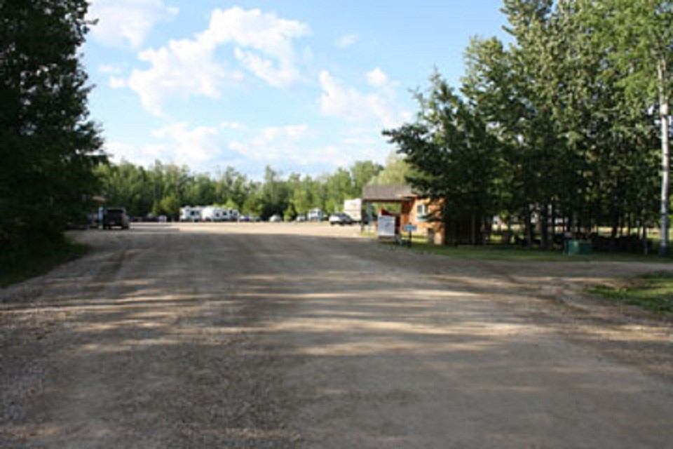 Unpaved campground road with parked trailers, trees, and small office building.