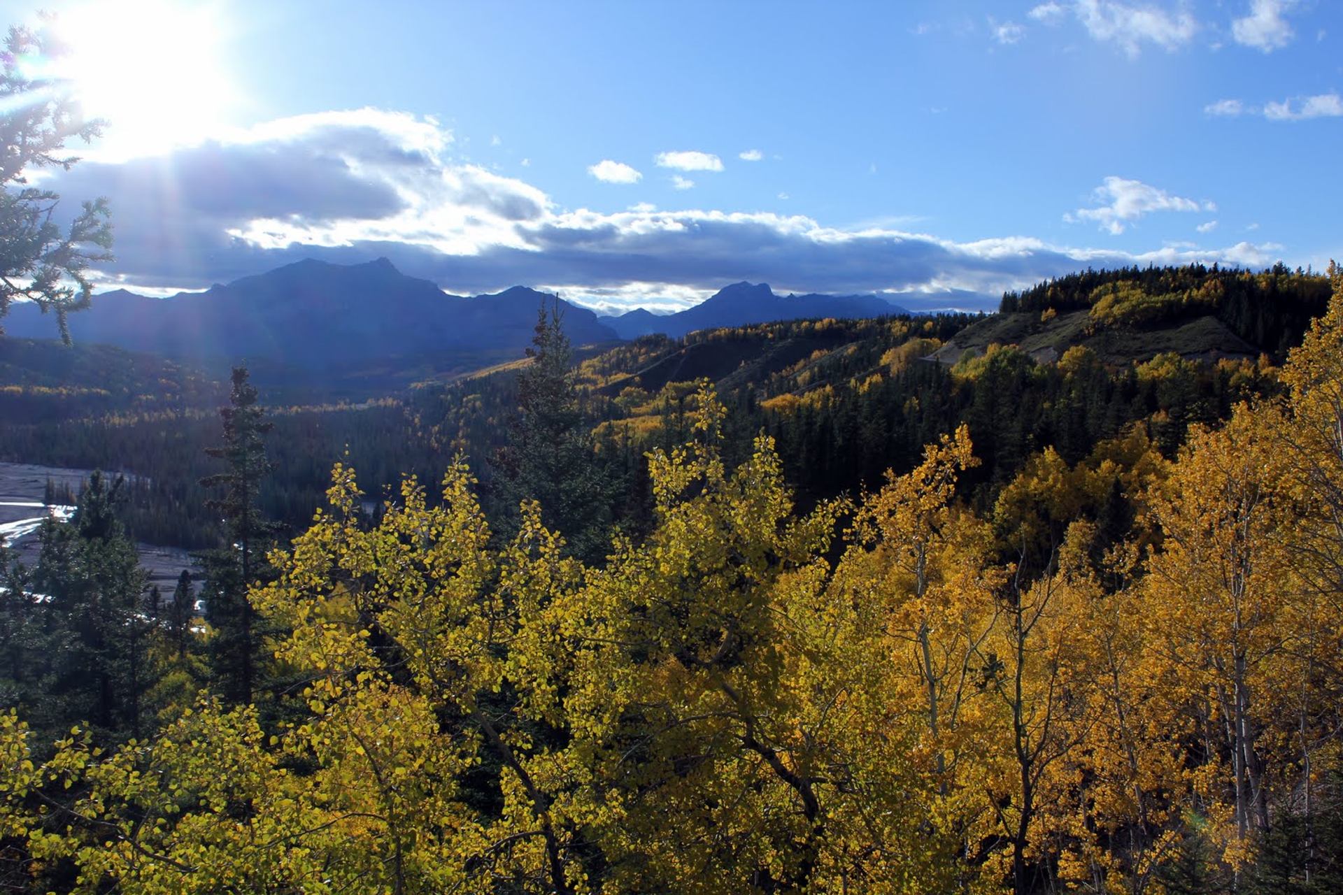 Sunlit mountain view with autumn trees and blue sky near Trembling Aspen Retreat.