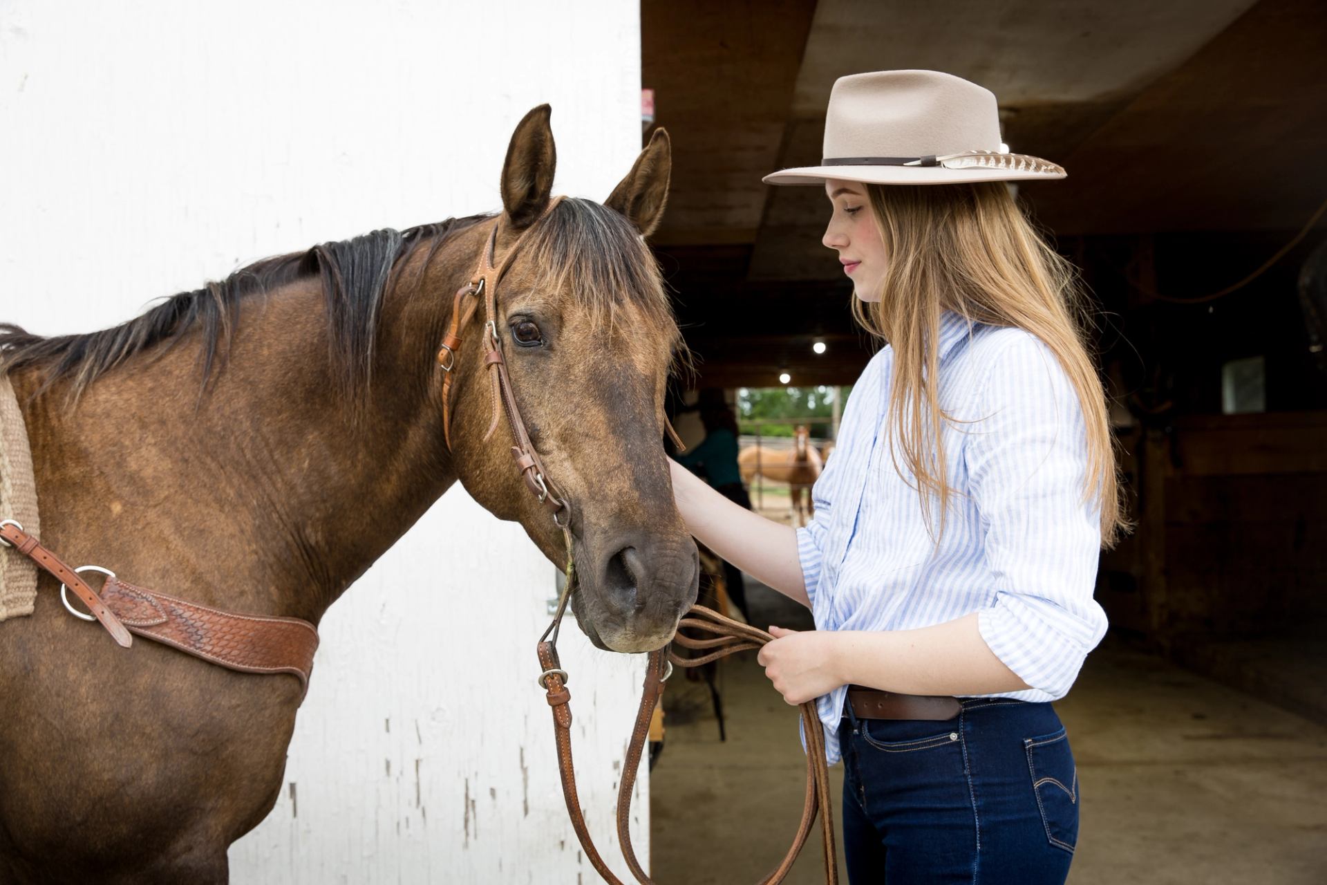 OH Ranch showcases a saddled horse beside a visitor near the entrance of a ranch barn.