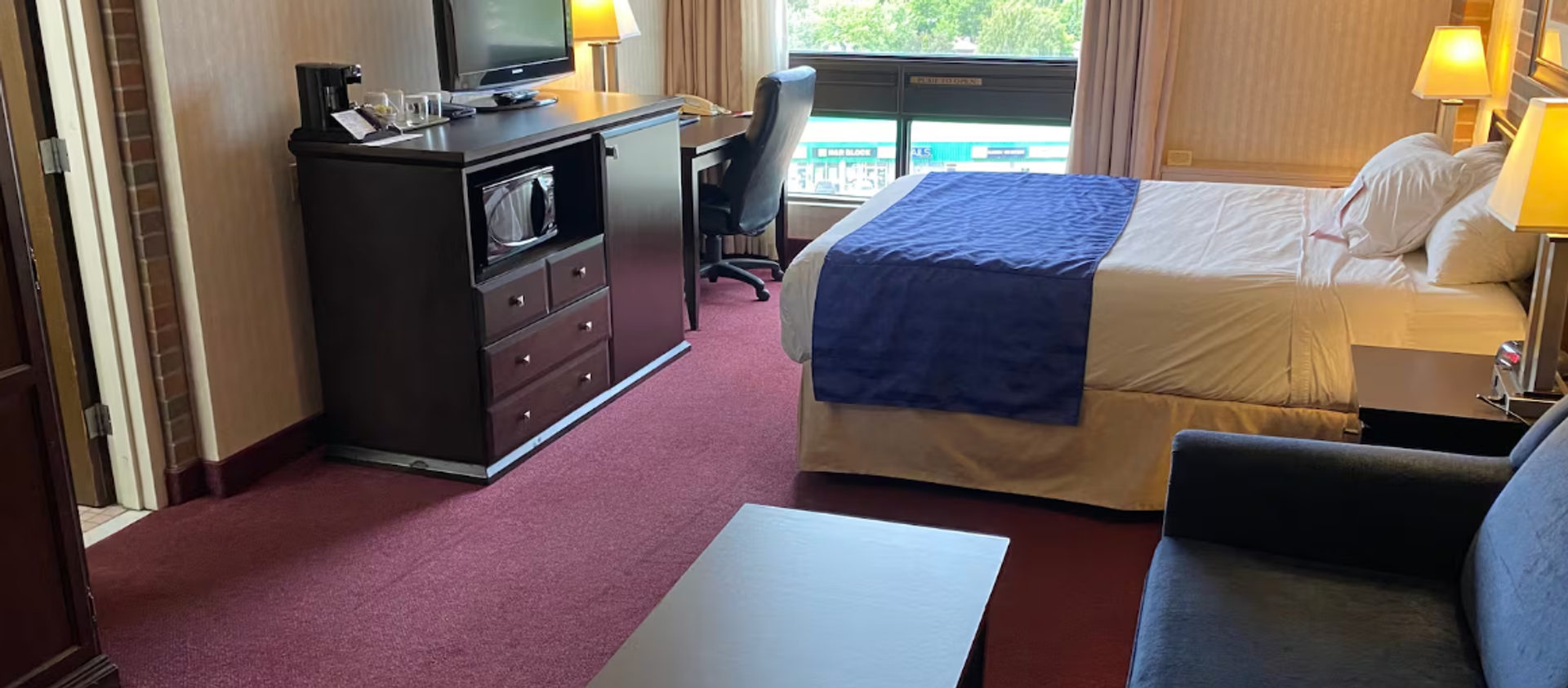 Hotel room with bed, desk, TV, microwave, and seating area.