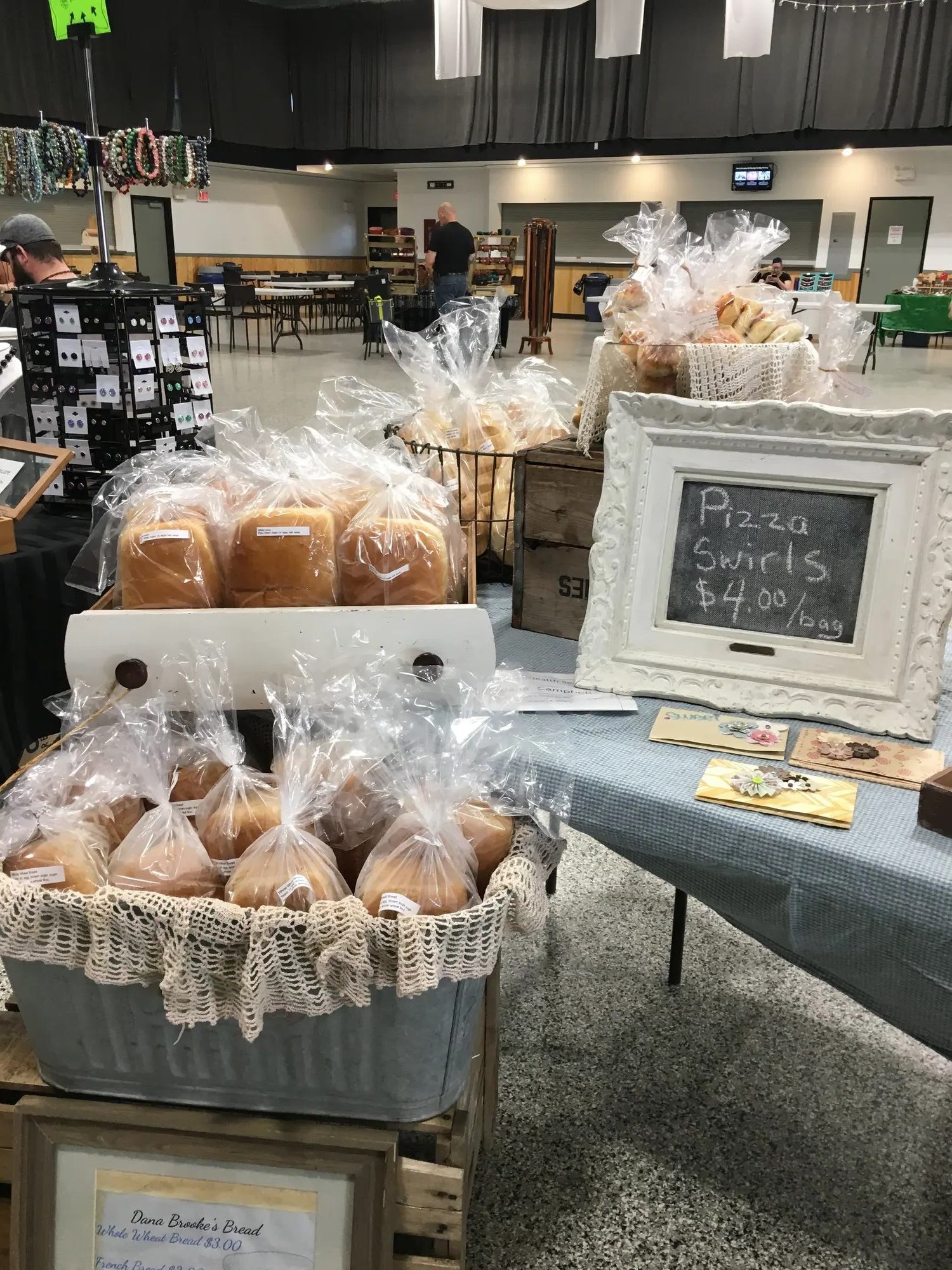 Market stall with bagged loaves of bread and pizza swirls sign on table.