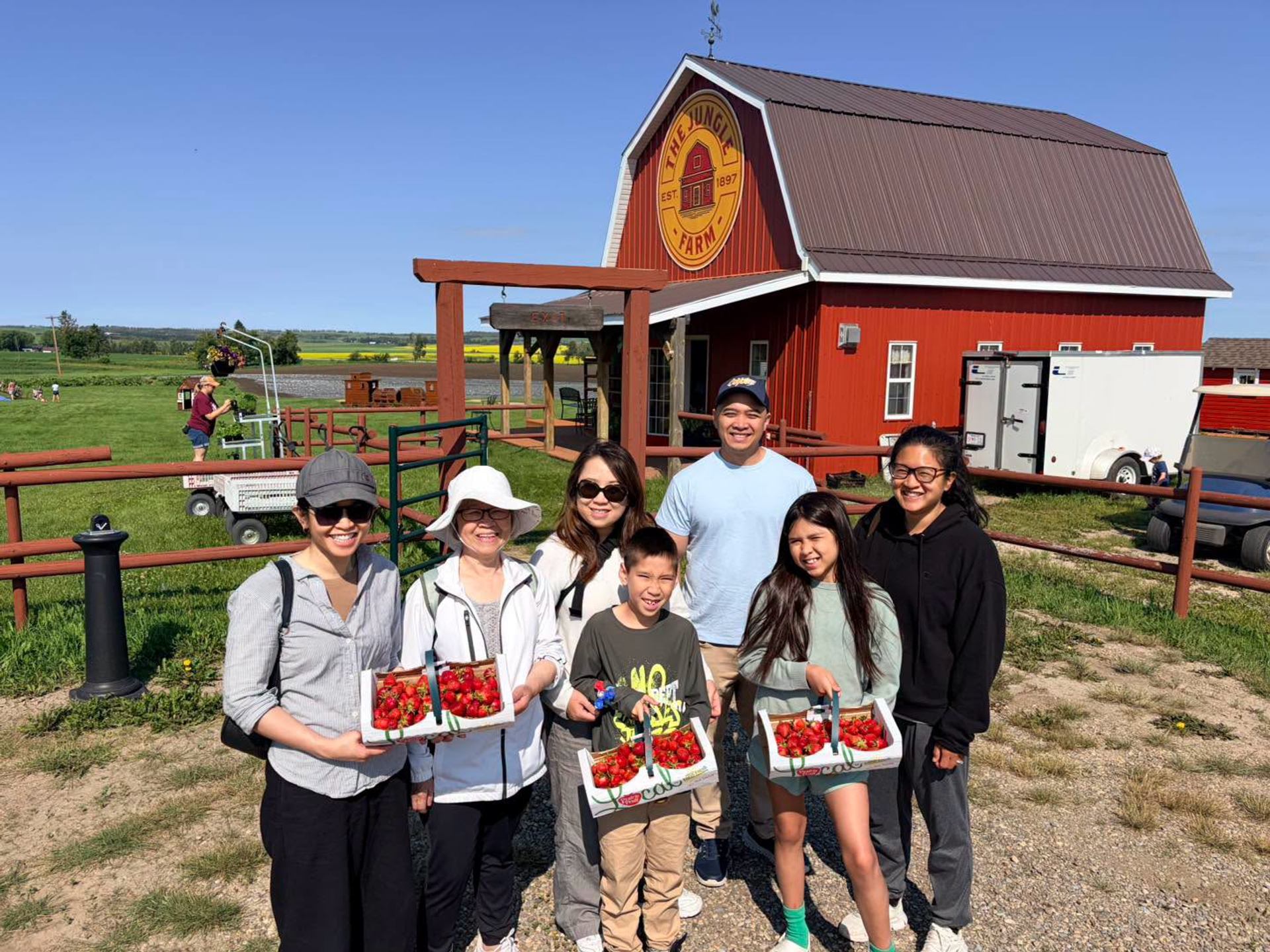 Group of people holding strawberry baskets in front of The Jungle Farm red barn.