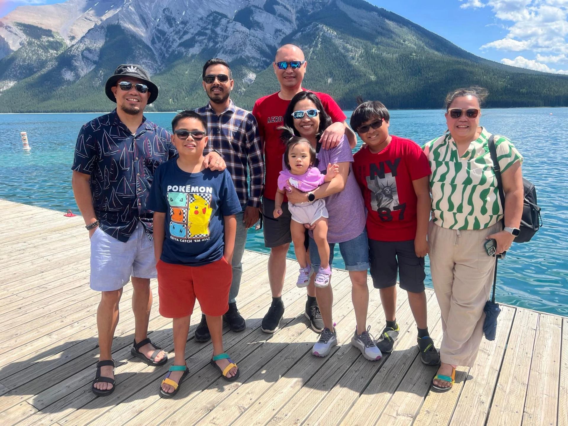 Group of people on wooden dock beside turquoise lake with forested mountains behind.