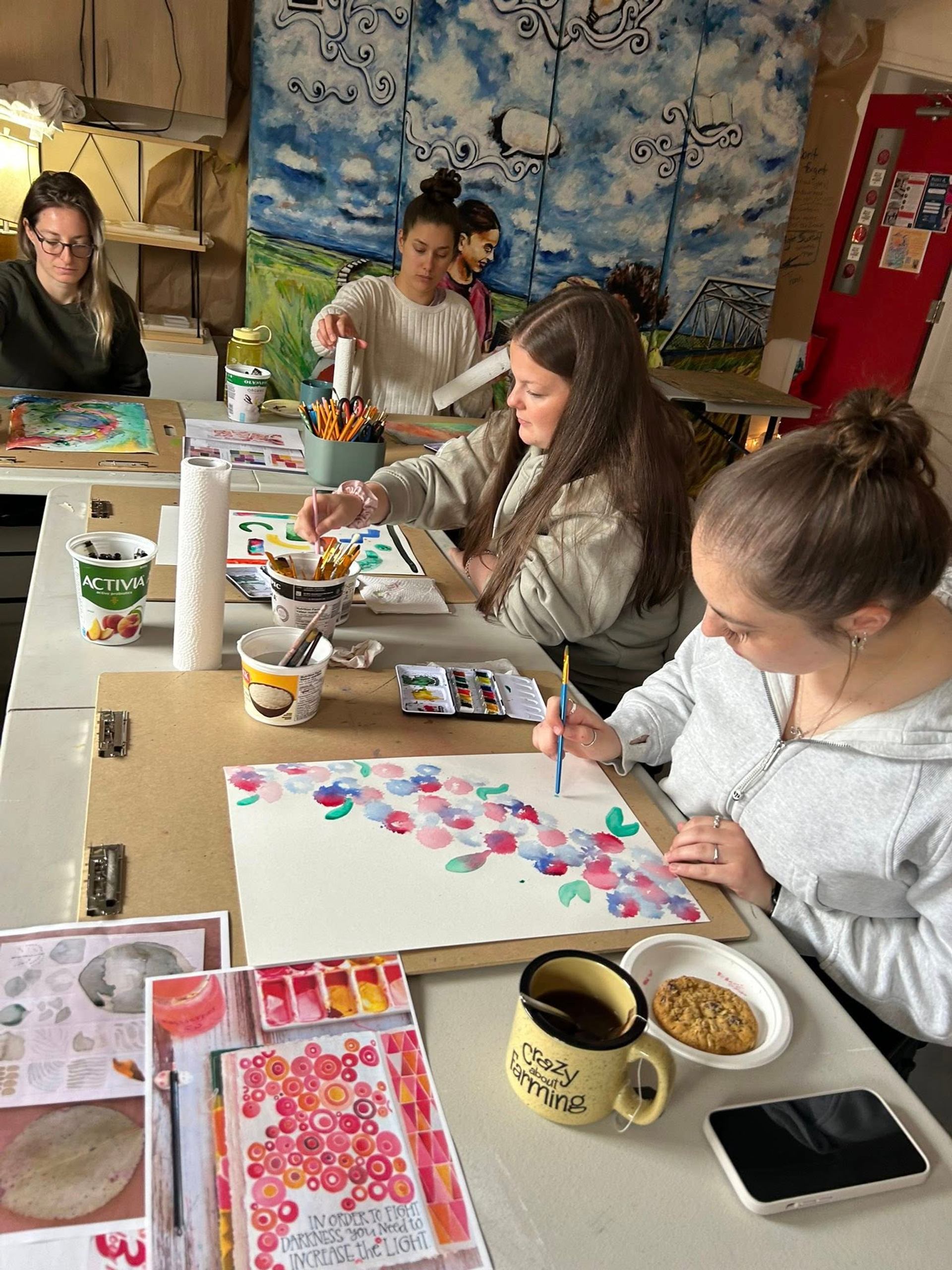 Group painting at table with colorful supplies and mural backdrop.