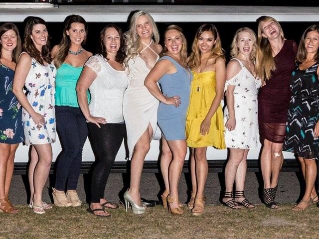 Group of ten posing in front of white limo at night, dressed for a celebration.