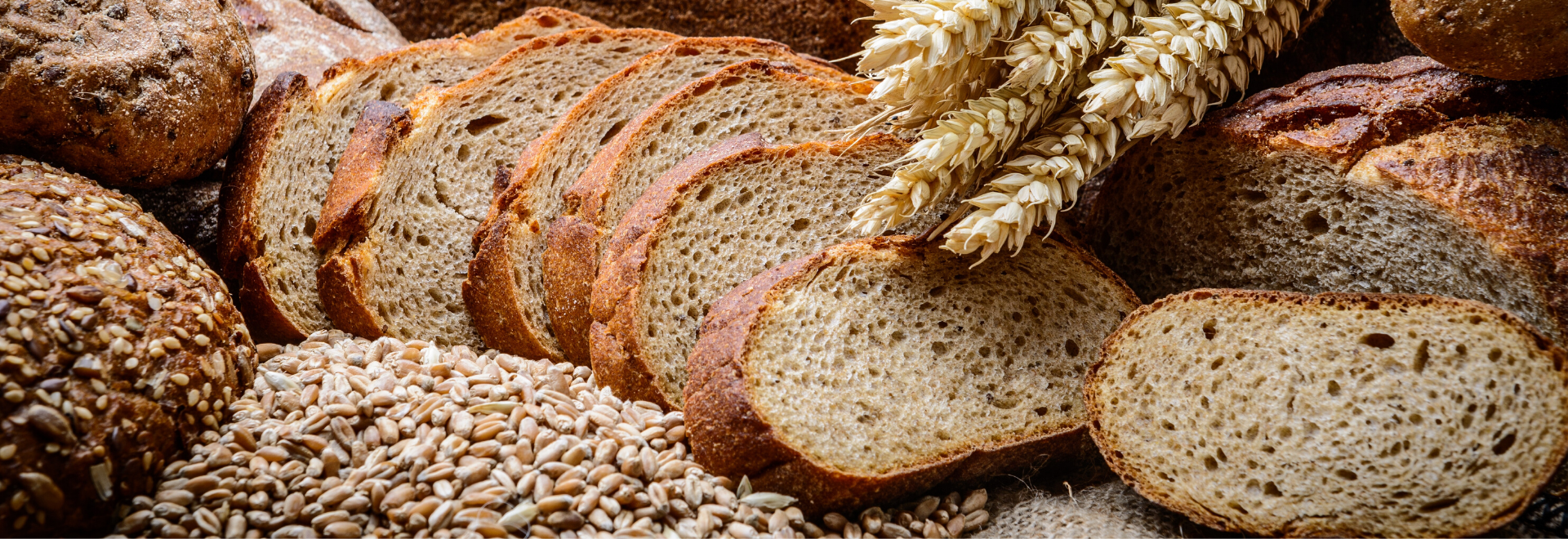 Sliced artisan bread, seeded loaves, wheat stalks, and grains are arranged for market display.