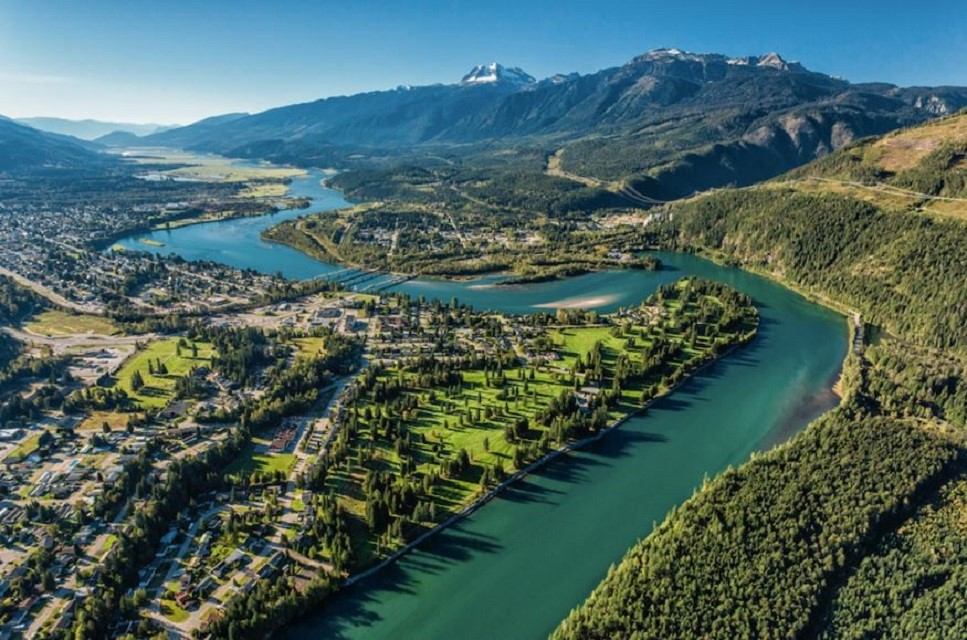River valley with trees, homes, and snowy mountains near Airport Shuttle Express Ltd.