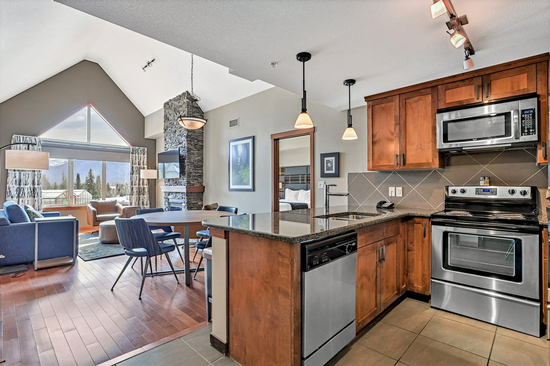 Open kitchen and living area with wood cabinetry, stainless steel appliances and stone fireplace.