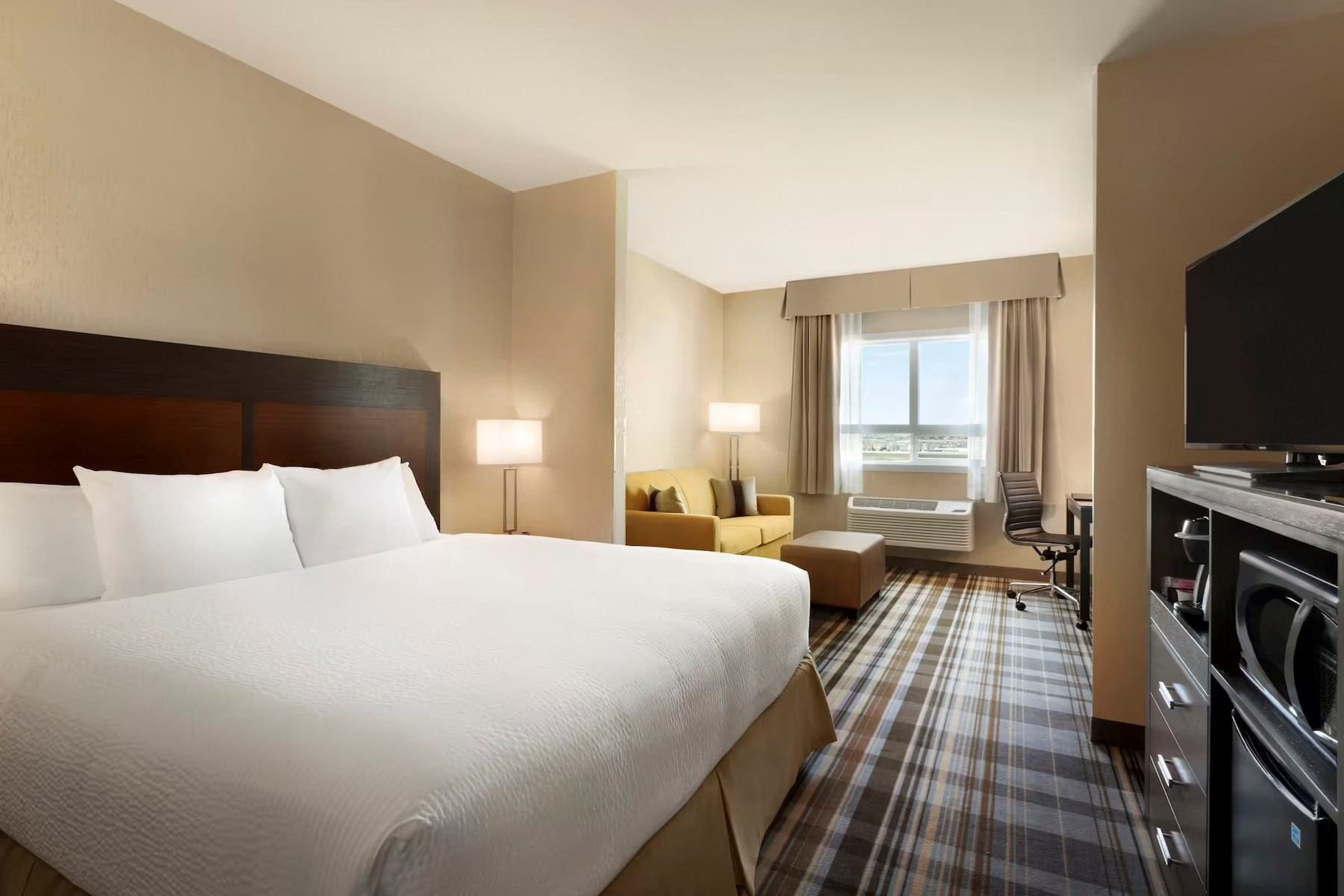 Hotel room with bed, seating, window, desk chair, and dresser with flat-screen TV.